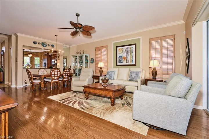 Living room featuring ceiling fan, crown molding, wood-type flooring, and suspended lighting