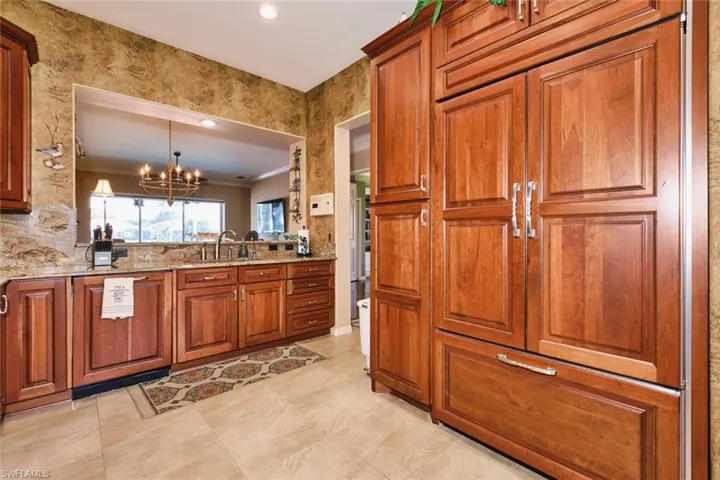 Kitchen with wood finish cabinetry, light stone counters, suspended lighting, dishwasher, and ornamental molding