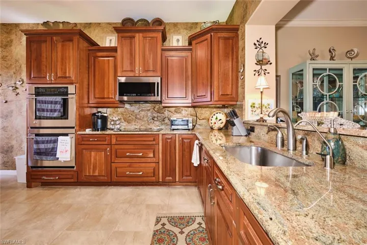 Kitchen with stainless steel appliances, wood finish cabinets, light stone counters, tasteful backsplash, and ornamental molding