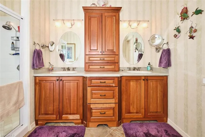 Full bath with double vanity, wallpapered walls, and a tile shower