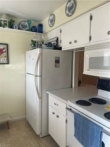 Kitchen with light countertops, freestanding refrigerator, light tile patterned flooring, white cabinetry, and range