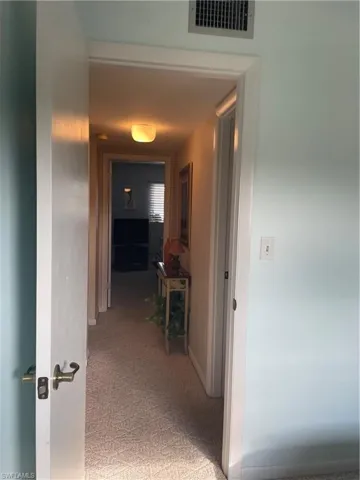 Hall with baseboards, visible vents, and light colored carpet