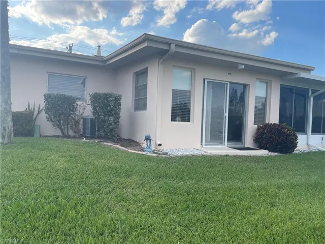 Rear view of property with central air condition unit, a lawn, and stucco siding