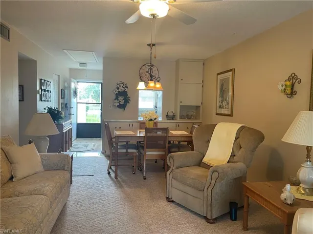 Living room with attic access, visible vents, a ceiling fan, and light colored carpet