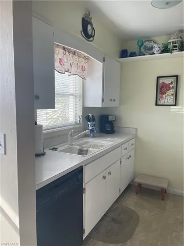 Kitchen featuring dishwashing machine, tile patterned flooring, light countertops, white cabinetry, and a sink