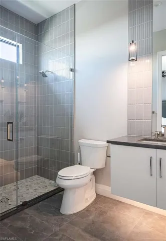 Full bath with vanity, toilet, a shower stall, baseboards, and marble finish flooring