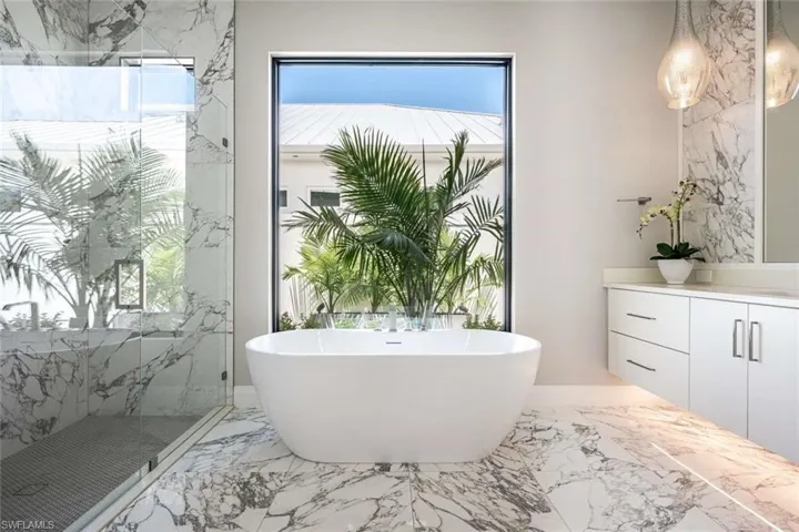 Bathroom with marble tiled flooring, a freestanding tub, vanity, and a marble finish shower