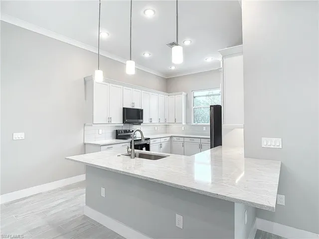 Kitchen featuring white cabinetry, kitchen peninsula, pendant lighting, black appliances, and sink
