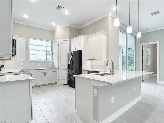 Kitchen with white cabinets, sink, black fridge, and plenty of natural light
