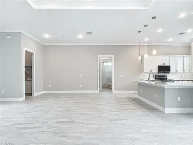 Kitchen featuring white cabinets, decorative light fixtures, crown molding, light stone countertops, and range with electric stovetop