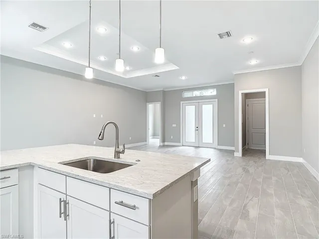 Kitchen with pendant lighting, light stone counters, sink, white cabinetry, and light hardwood / wood-style flooring