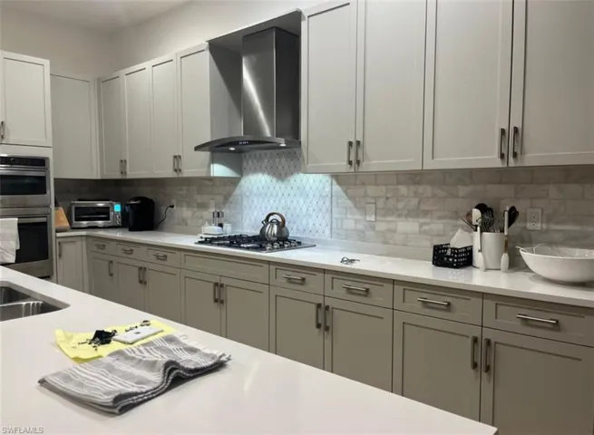 Kitchen with wall chimney range hood, decorative backsplash, stainless steel appliances, and light stone counters