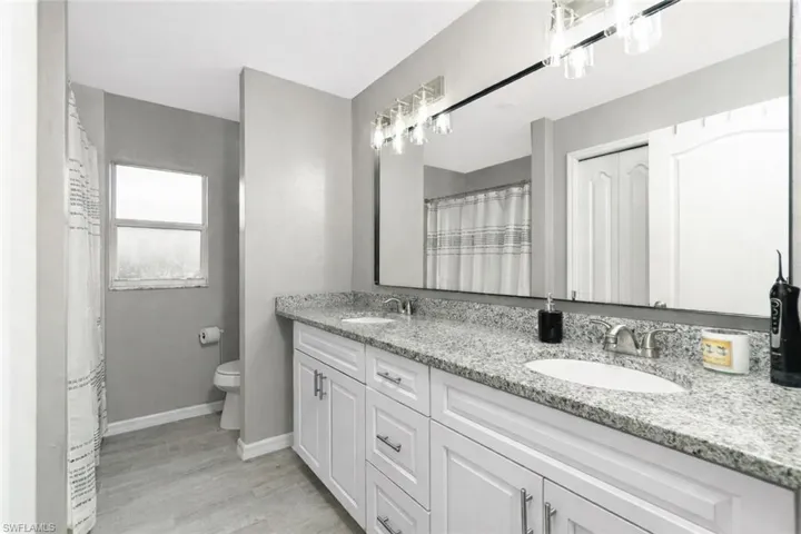 Full bath with double vanity, curtained shower, light wood-style flooring, and a closet