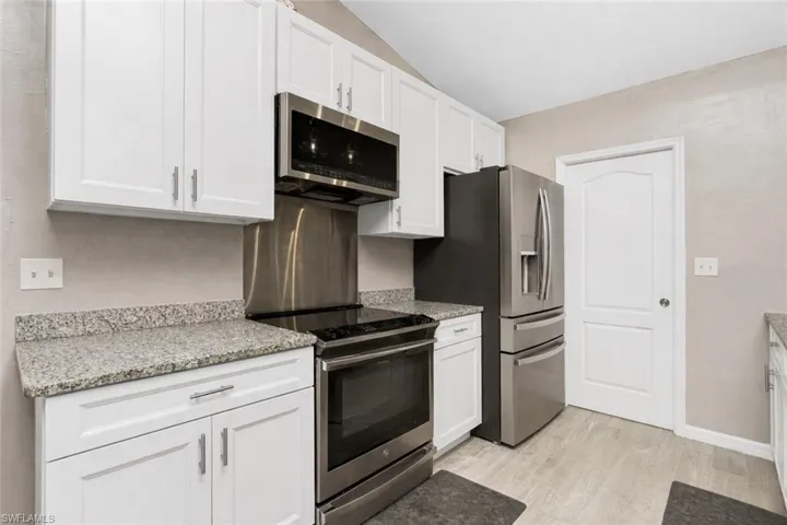 Kitchen with stainless steel appliances, white cabinets, and light stone countertops