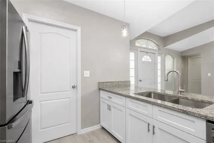 Kitchen with stainless steel fridge, light stone counters, white cabinetry, pendant lighting, and light wood-type flooring