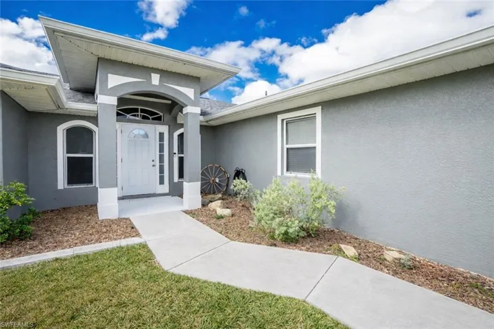 View of exterior entry with stucco siding and a yard