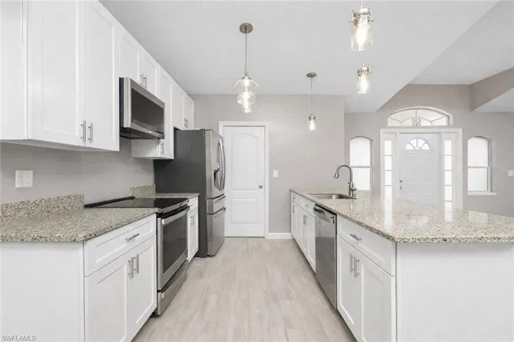 Kitchen with stainless steel appliances, white cabinetry, light stone countertops, light wood-style flooring, and hanging light fixtures