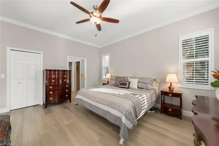 Primary Bedroom with crown molding, a ceiling fan, a walk-in closet, light wood finished floors, and an-ensuite bathroom