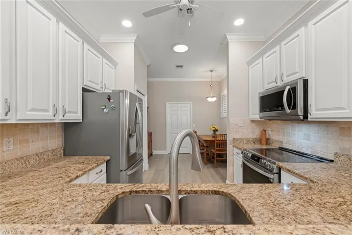 Kitchen featuring backsplash, stainless steel appliances, white cabinets, crown molding, and decorative light fixtures