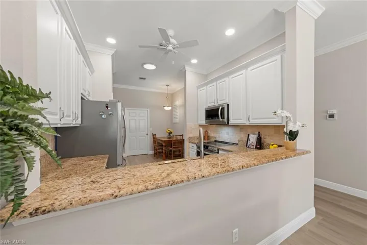 Kitchen with light stone countertops, white cabinets, light wood finished floors, appliances with stainless steel finishes, and ornamental molding