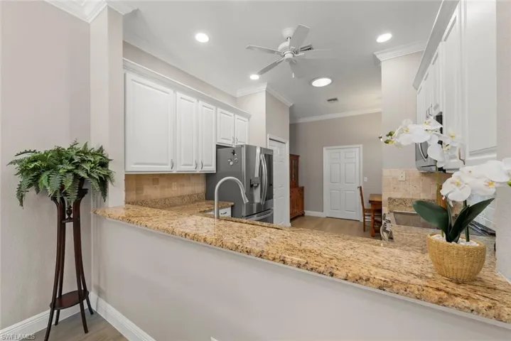 Kitchen featuring backsplash, stainless steel appliances, light wood finished floors, light stone countertops, and crown molding