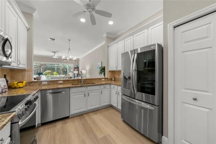 Kitchen with ceiling fan, stainless steel appliances, light wood-style floors, white cabinets, and crown molding