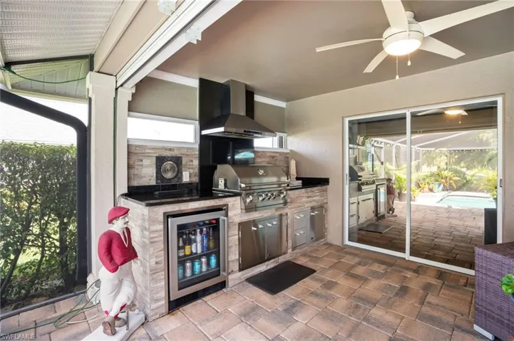 Outdoor kitchen features upscale grill, beverage cooler, stainless steel fridge, and stainless steel range hood