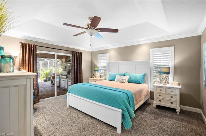 The spacious primary bedroom is highlighted by try ceiling, sitting area, Bahama shuttered windows allowing for adjustable natural lighting and sliding glass doors to the pool and lanai area.