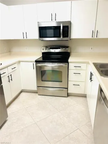 Kitchen featuring light tile patterned floors, white cabinets, appliances with stainless steel finishes, and sink