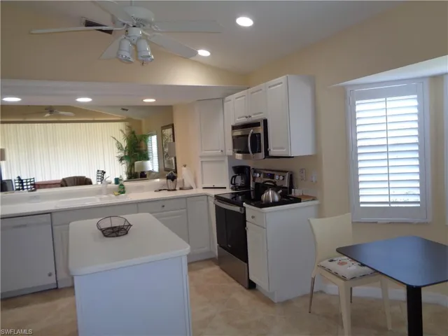 Kitchen featuring stainless steel appliances, vaulted ceiling, light countertops, white cabinets, and a kitchen island