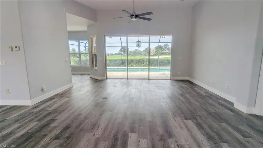 Unfurnished room featuring lofted ceiling, a healthy amount of sunlight, ceiling fan, and dark hardwood / wood-style floors