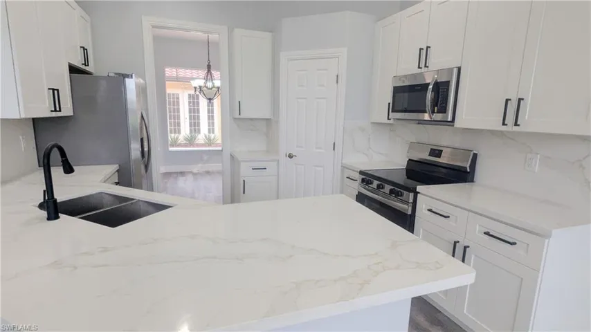 Kitchen featuring appliances with stainless steel finishes, a chandelier, white cabinetry, and sink