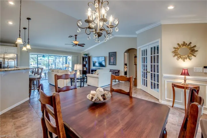 Dining room with crown molding, a ceiling fan, arched walkways, light stone finish floors, and lofted ceiling