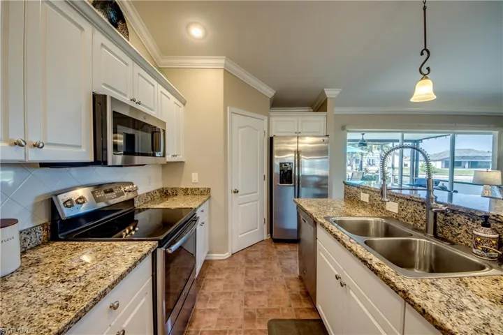 Kitchen featuring stainless steel appliances, decorative backsplash, white cabinetry, decorative light fixtures, and ornamental molding