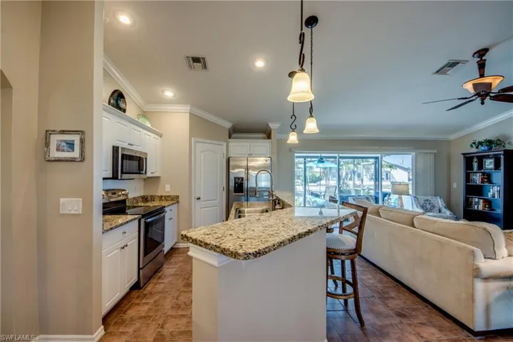 Kitchen featuring crown molding, stainless steel appliances, white cabinetry, light stone countertops, and pendant lighting