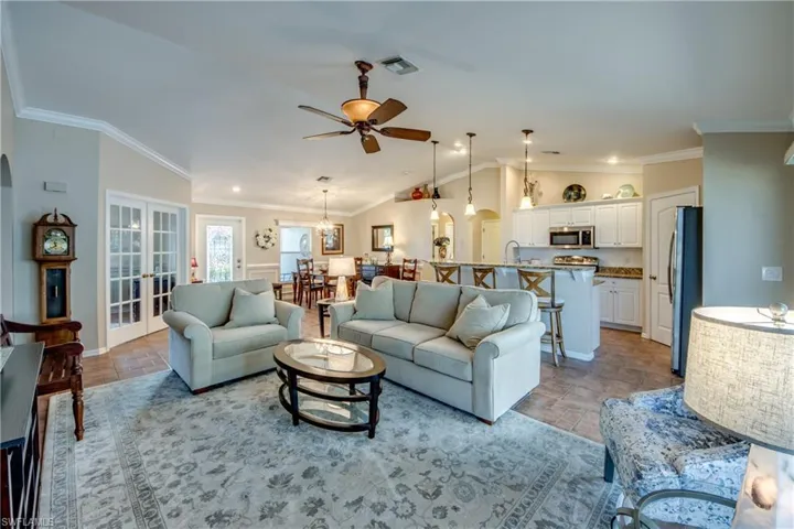 Living area featuring lofted ceiling, a ceiling fan, crown molding, light stone finish flooring, and hanging lights