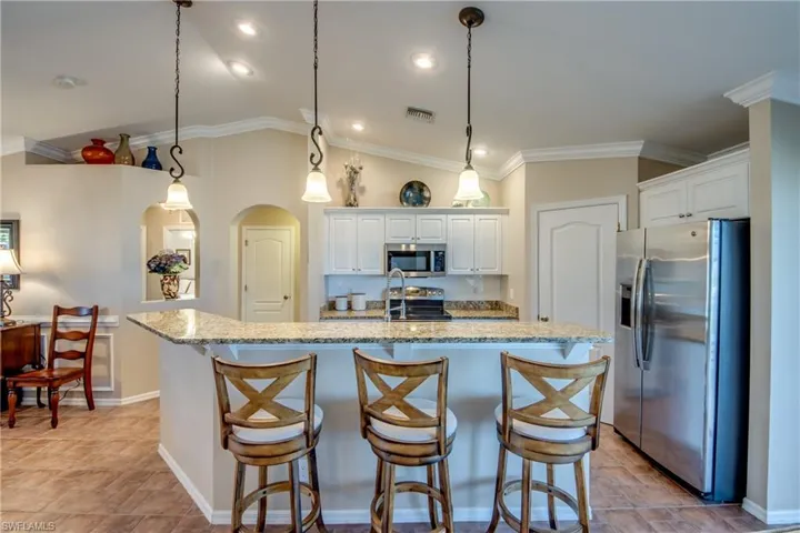 Kitchen with stainless steel appliances, white cabinetry, light stone countertops, vaulted ceiling, and crown molding