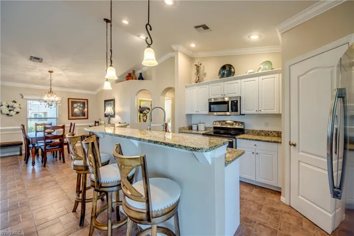 Kitchen with lofted ceiling, white cabinets, stainless steel appliances, ornamental molding, and light stone counters