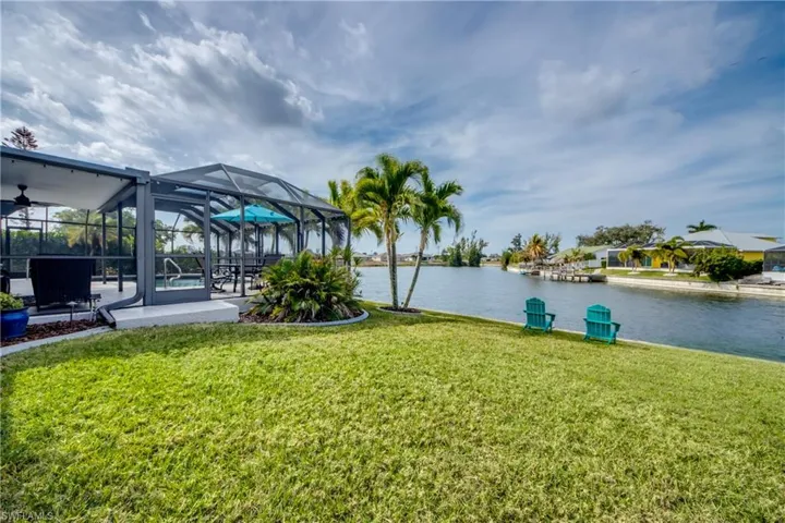 View of green lawn featuring a sunroom, a lanai, a patio area, a water view, and ceiling fan