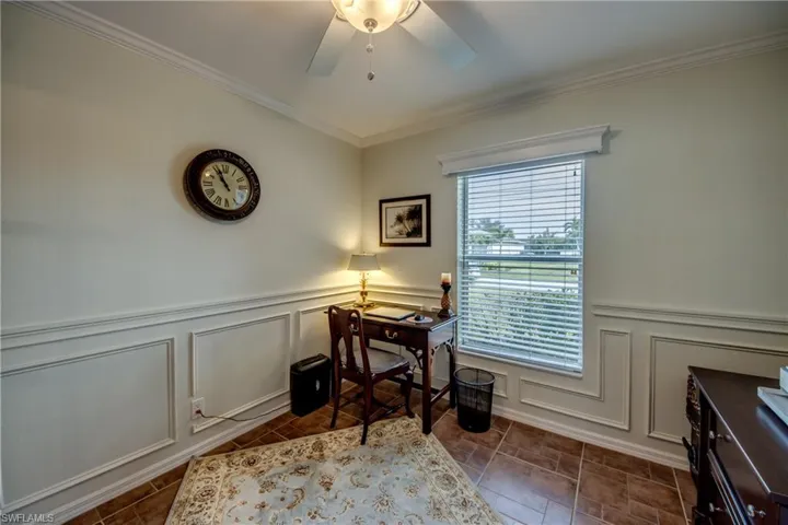 Office space with crown molding, a ceiling fan, wainscoting, and a decorative wall