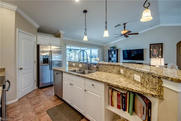 Kitchen featuring white cabinets, ornamental molding, pendant lighting, stainless steel appliances, and light stone counters