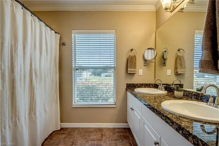 Full bath featuring ornamental molding, double vanity, curtained shower, and light stone finish flooring