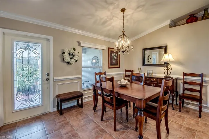 Dining area featuring crown molding, suspended lighting, a wainscoted wall, stone finish flooring, and vaulted ceiling