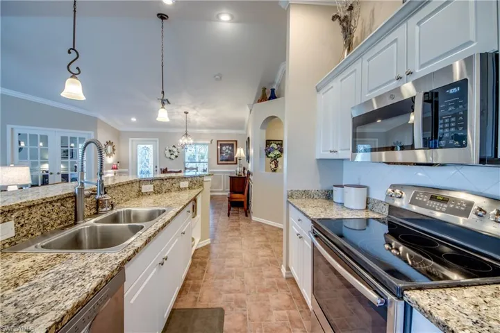 Kitchen with stainless steel appliances, hanging light fixtures, white cabinets, ornamental molding, and decorative backsplash