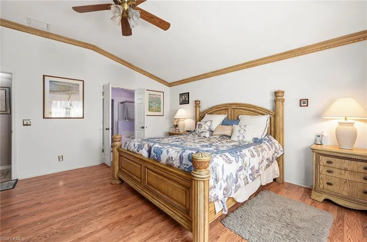 Bedroom with ornamental molding, wood finished floors, vaulted ceiling, a ceiling fan, and connected bathroom