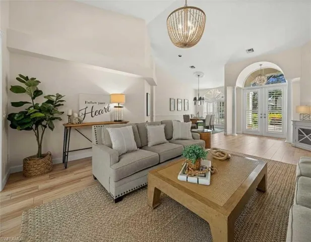 Living room with french doors, a chandelier, light wood finished floors, and vaulted ceiling
