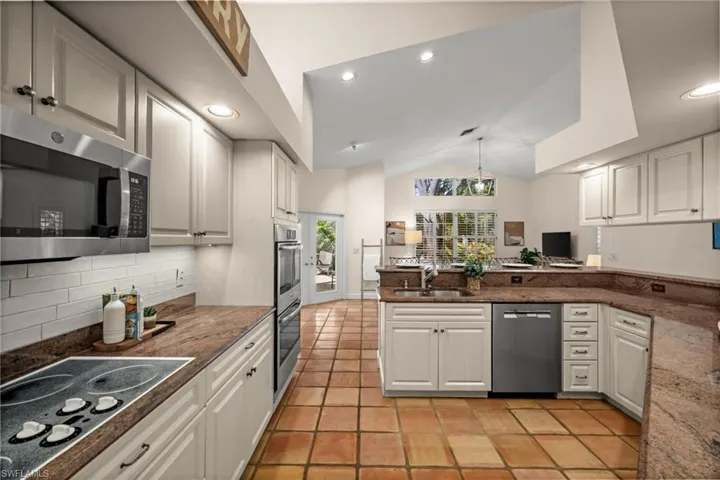 Kitchen with lofted ceiling, appliances with stainless steel finishes, decorative light fixtures, a peninsula, and dark stone countertops