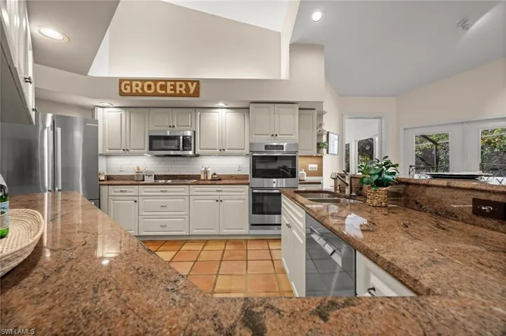 Kitchen with stainless steel appliances, dark stone counters, recessed lighting, decorative backsplash, and high vaulted ceiling