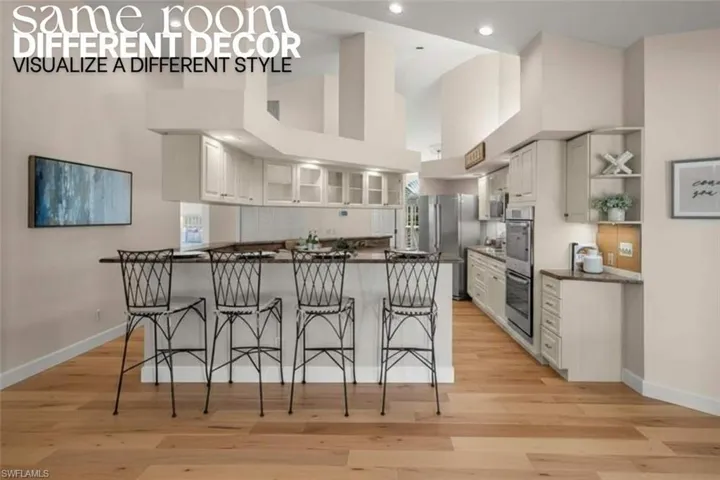 Kitchen with dark countertops, a breakfast bar, open shelves, appliances with stainless steel finishes, and light wood-style flooring