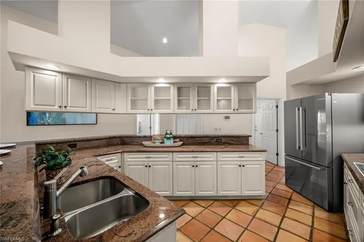 Kitchen with glass insert cabinets, freestanding refrigerator, high vaulted ceiling, dark stone countertops, and white cabinetry